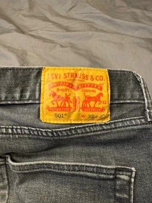 Levi's 501 grå jeans W32 L32 - Säljer ett par klassiska Levi's 501 jeans i grå tvätt med raka ben och fem fickor. Jeansen har en ikonisk läderpatch bak i midjan och den röda Levi's-taggen på bakfickan. Materialet är slitstarkt denim i bomull och passformen är normal.