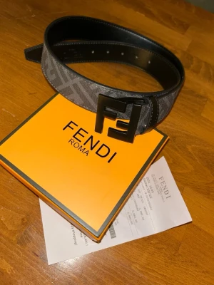Fendi bälte med FF-spänne - Säljer ett snyggt Fendi-bälte i grått med klassiskt FF-mönster och ett stort svart FF-spänne. Nytt aldrig använt, storlek 85