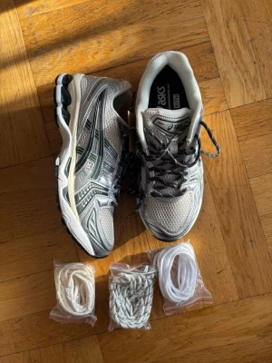 Asics Gel-Kayano 14 x Kith sneakers - Säljer ett par Asics Gel-Kayano 14 x Kith sneakers i silver och svart med mesh och syntetmaterial. Skorna har rund tå, platt sula och kommer med tre extra skosnören i olika färger. Snygg retrostil med coola detaljer och Kith branding på hälen.