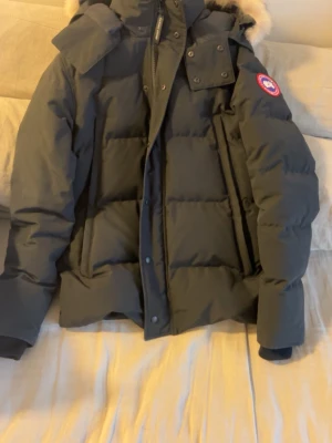 Canada Goose Wyndham Parka - Nu är det dags att sälja min Canada Goose Wyndham Parka. Jackan är inköpt för ungefär fem år sedan men är i riktigt bra skick. Väl omhändertagen då den är sparsamt använd. Äkthetsbevis finns på jackan så det är inga konstigheter. Storlek M. Pälsen är även avtagbar. Se bilderna för äkthetsbevis. 