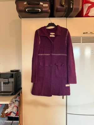 Lila lång kofta Odd Molly stickad - Säljer en snygg lila stickad kofta från Odd Molly med stora krage, dekorativa knappar och fickor framtill. Koftan har långa ärmar och coola vita detaljer längs axlar och midja. Perfekt för dig som gillar unika plagg med lite edge. Storlek 1 som enligt deras storleksguide motsvarar en storlek S. SAMPLE, kan vara något större i armhålorna.  Mycket fint skick, jag hittar inga synliga anmärkningar eller defekter.  