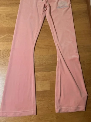 Rosa Y2K Juicy Couture - Säljer ett par ljusrosa mjukisbyxor från Juicy Couture i storlek S. Byxorna har bootcut-snitt, snörning i midjan och är gjorda i mjuk velour med broderad krona och logga framtill. Gick ner drastiskt i vikt efter jag köpte dem prislapp kvar på byxorna.