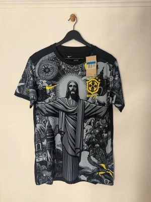 Nike Brazil Dri-Fit t-shirt med tryck - Snygg svart och grå t-shirt från Nike med Brasil-logga och stort grafiskt tryck av Kristusstatyn och detaljerade illustrationer. Har tagit av tagsen men har sparat dem. Tveka inte att skriva till mig!