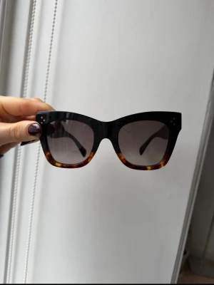 Svart och brun Celine Paris solglasögon - Snygga solglasögon från Celine Paris (New Audrey) med breda svarta bågar och brunmelerad kant. Modellen är CL4004IN och tillverkad i Italien. Glasen är mörka och bågarna har en cool, lite kantig form som ger en trendig vibe.