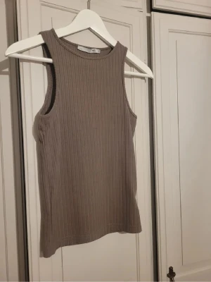 Ribbad beige linnetopp från 157 - Säljer en ribbad beige linnetopp från 157 i storlek S. Toppen är ärmlös med rund halsringning och har en slim passform. Materialet är mjukt och stretchigt, perfekt för varma dagar. Enkel och stilren design som funkar till många olika looks. Använd 1 gång.