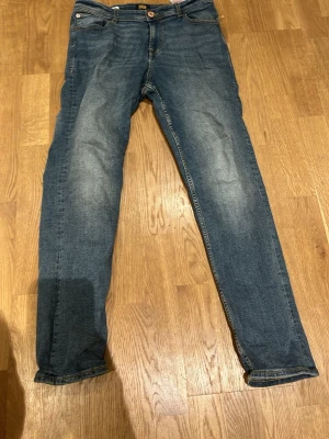 Blå jeans från Jack & Jones regular - Säljer ett par klassiska blå jeans från Jack & Jones i regular fit. Jeansen har fem fickor, gul kontrastsöm och knappstängning framtill. Materialet är slitstarkt denim och passformen är rak med normal midja. Perfekt för dig som gillar enkel och tidlös stil.