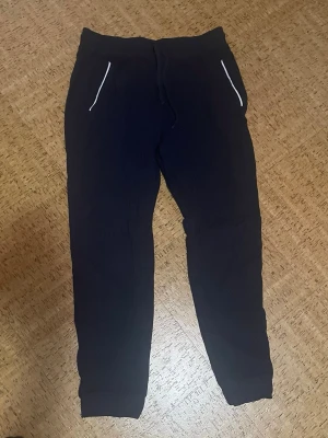 Svarta mjukisbyxor - Svarta mjukisbyxor med vita detaljer vid fickorna. Byxorna har en avslappnad passform och är tillverkade i mjukt bomullsmaterial. Perfekta för chill eller träning.