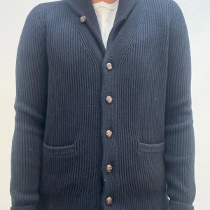 Mörkblå ribbad kofta med knappar - Snygg mörkblå ribbstickad kofta med stora knappar framtill och två fickor. Koftan har lång ärm och en klassisk krage, perfekt för lager-på-lager-stil. Materialet är stickat och ger en mysig känsla.