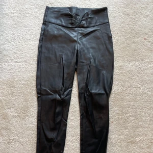 Svarta skinnbyxor från Zara, stl S - Snygga svarta skinnbyxor från Zara i storlek S. Byxorna är högmidjade med smal passform och har dragkedja vid benslut. Tillverkade i syntetmaterial med en matt finish och diskret rynkdetalj framtill i midjan.