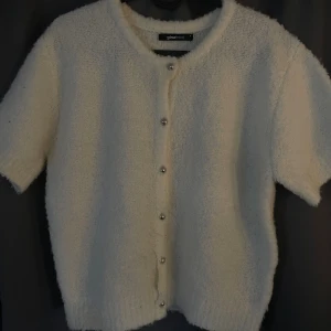 Vit kofta med pärlknappar från Gina Tricot - Supermjuk och fluffig vit kofta från Gina Tricot med korta ärmar och rund hals. Koftan har snygga pärlknappar framtill och är gjord i ett stickat material som känns riktigt cozy. Tyvärr har det blivit ett hål som man ser på andra bilden, det syns inte jätte mycket på och går att sy igen för den som vill det. Annars jätte fin och perfekt till hösten. Helt slutsåld, säljs för att den inte kommer till användning. 