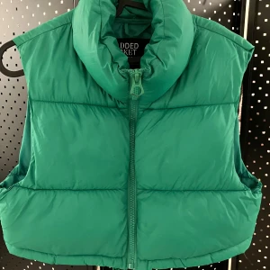 Grön dunväst från Stradivarius XS - Cool grön dunväst från Stradivarius i storlek XS. Västen har hög krage, quiltad design och dragkedja framtill. Perfekt för lager-på-lager och ger en sportig vibe till din outfit.