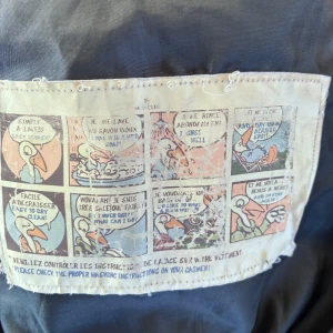 Mörkblå lång dunjacka från Moncler - Säljer en mörkblå lång dunjacka från ”Moncler” med huva och snygga spännen i midjan, bältet är avtagbart. Jackan har dragkedja, ribbade muddar och klassisk Moncler-logga på ärmen. Perfekt för kalla dagar och riktigt stilren look. Vet ej äkthet, kan inte sånt har fått den av en vän och den har några år på nacken men fint skick. Dragsnören kan behöva bytas. Liten skada längst ner på sidan se bild . Skulle säga som en storlek Medium.