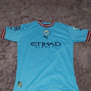 Manchester City Haaland matchtröja Puma - Manchester Citys officiella ljusblå matchtröja med Haaland 9 på ryggen. Tröjan har röda och vita detaljer vid ärmslut och krage, Premier League-märke på ärmen och Etihad Airways-tryck på bröstet. Tillverkad i lätt och ventilerande polyester.