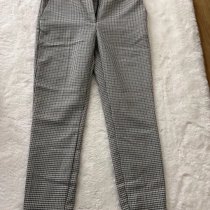Svartvita rutiga kostymbyxor - Snygga kostymbyxor med svartvitt rutigt mönster. Byxorna har en rak passform och klassisk midja. Perfekta för dig som vill ha en stilren och trendig look. Materialet känns mjukt och följsamt, vilket gör dem bekväma hela dagen.