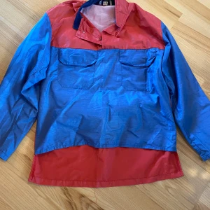 Retro vindjacka/overshirt  - Cool overshirt från Raket i blått och rött med lång ärm, två stora bröstfickor och meshfoder. Skjortan har tryckknappar vid kragen blå detaljer.