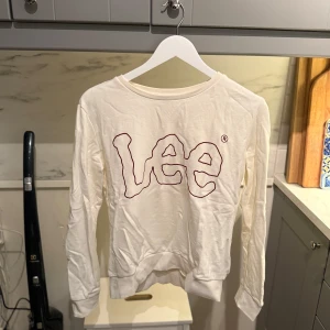 Vit långärmad tröja från Lee - Säljer en vit långärmad tröja från Lee med stort broderat logotyptryck i vinrött framtill. Tröjan är tillverkad i mjuk bomull. Tröjan är skrynklig på bilen, men stryker den såklart ifall någon är intresserad av att köpa den!🤩.