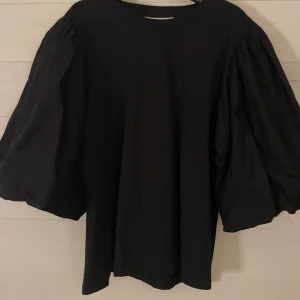 Svart topp med puffärmar från Vila - Svart topp från Vila med riktigt stora puffärmar som ger en cool och trendig siluett. Rund halsringning och rak passform. Perfekt för dig som vill sticka ut lite extra med en enkel men snygg look.