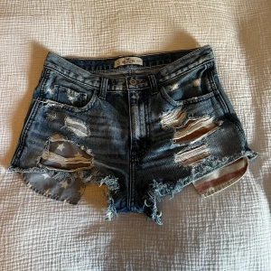 Jeansshorts från Hollister - Säljer dessa blå jeansshorts ifrån Hollister med råa kanter & slitningar i storlek W27. De har många coola detaljer både fram & bak (se bilderna)💘         De bedöms vara i mycket fint skick men!                  Skickar ditt köp inom 24h!💘                                       De är bara att skriva om de är något ni vill veta.🥰