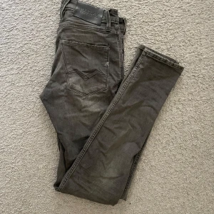 Grå Replay jeans, modell Anbass W28 L32 - Säljer ett par grå jeans från Replay, modell Anbass. De är raka i modellen och tillverkade i mjukt jeanstyg med lite stretch för extra komfort. Riktigt sköna! Den enda defekten är att läderlappen på baksidan har lossnat lite som man ser på sista bilden. Hör av er vid funderingar!