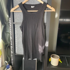 Svart ribbad linnetopp XS - En svart ribbad linnetopp i storlek XS. Toppen har en klassisk rak passform med breda axelband och rund halsringning. Perfekt att styla med jeans eller kjol för en enkel och clean look.