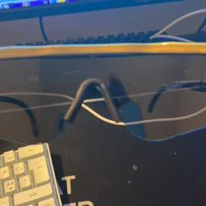 Guldiga pitvipers-solglasögon med spegelglas - Säljer ett par feta shield-solglasögon från Vetements med guldiga detaljer och spegelglas. De har en futuristisk vibe med bred båge och svart näskuddar. Perfekta för dig som vill sticka ut och köra en sportig look.