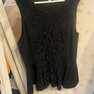 Svart spetsblus  - Säljer en svart ärmlös blus från Stockholm i storlek L. Toppen har vacker spets framtill och baktill, med en lätt utställd nederdel. Perfekt för dig som gillar stilrena och feminina detaljer.