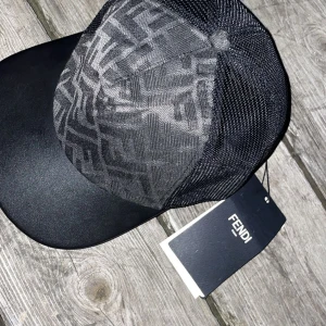 FENDI Svart keps - Snygg svart keps från Fendi med ikoniskt FF-mönster i grått på framsidan. Kepsen har mesh-paneler på sidorna och baksidan för extra ventilation samt böjd skärm i svart. Märkeslapp sitter kvar. Perfekt accessoar för en trendig streetstyle. Storlek M passar S 
