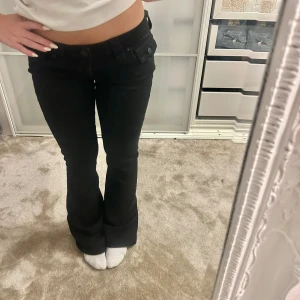 Svarta bootcut jeans True Religion - Svarta jeans från True Religion med bootcut passform och klassiska fickor med lock och knapp bak. Snyggt lågmidjade och. Perfekta för dig som gillar en tidlös och cool look. De är lite sönder där nere