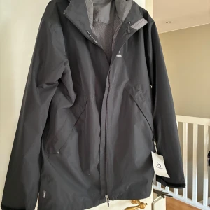 Helt ny Svart vindjacka från Haglöfs M - Säljer en svart vattentät vindjacka från Haglöfs i storlek M. Jackan har dragkedja, meshfoder och två snedställda fickor med dragkedja. Snygg och funktionell design med hög krage och justerbar huva. Inköpt i fel storlek- så aldrig använd. 