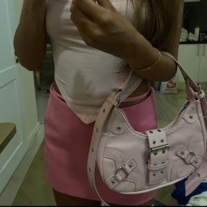 Ljusrosa väska i läderimitation  - Snygg rosa väska  med enkel tuff design. passform. Liknar typ Balenciagas modell. Skitsnygg och passar till det mesta. Använd 1 gång.