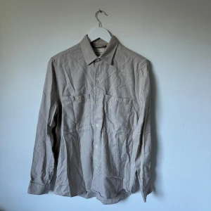 Beige överskjorta från A Day's March - Stilren beige överskjorta från A Day's March i 100% bomull. Skjortan har klassisk krage, två bröstfickor med knappar och långa ärmar. Perfekt för en clean och avslappnad look. Tillverkad i Portugal. 2Å9