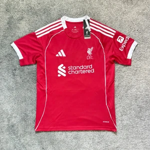 Liverpool Salah 11 Adidas matchtröja M - Liverpool FC fotbollströja i rött med vita detaljer, Adidas-logga och broderat klubbmärke. Nummer 11 och M. Salah på ryggen. Slim fit, kortärmad och tillverkad i ventilerande polyester. Klassisk design med vita ränder på axlarna och sponsortryck framtill.
