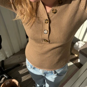 Beige/brun ribbad långärmad tröja med knappar - Säljer en beige/brun ribbad långärmad tröja med snygga knappar framtill. Tröjan har en figurnära passform och är tillverkad i ett stretchigt material som sitter skönt på kroppen.  Så himla fin och mysig nu till lite kyligare tider😍😍