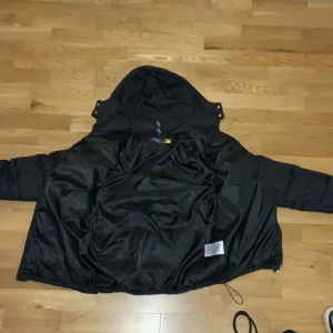 Svart pufferjacka från Polo Ralph Lauren - Säljer en svart pufferjacka från Polo Ralph Lauren med huva och dragkedja framtill. Jackan har det klassiska röda Polo-logot broderat på bröstet och flera praktiska fickor. Perfekt för kyliga dagar och riktigt snygg streetstil.
