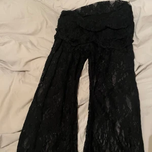 Svarta vida spetsbyxor - Säljer ett par svarta byxor i transparent spets med blommönster och hög midja. Byxorna har en loose och wide passform med snyggt fall och är perfekta för dig som vill sticka ut. Materialet är lätt och luftigt, vilket ger en cool vibe.