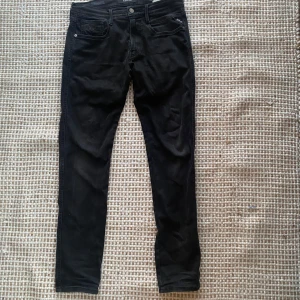 Svarta Replay Anbass jeans, stl 33 - Svarta Replay Anbass jeans i slim fit med klassisk femficksdesign och diskret logga på bakfickan. Jeansen har en smal passform och är tillverkade i mjukt denimtyg som sitter snyggt. Perfekta för dig som gillar stilrena och bekväma jeans.