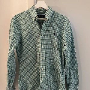 Rutig skjorta från Ralph Lauren S - Säljer en slim fit skjorta från Ralph Lauren i storlek S. Skjortan är rutig i grönt, blått och vitt med klassisk button down-krage och broderad logga på bröstet. Tillverkad i 100% bomull och har långa ärmar samt knäppning framtill. Priset går att diskutera 
