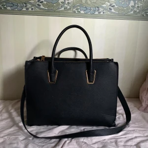 Svart axelväska med gulddetaljer - Skriv ifall mått på väskan önskas. Svart axelväska i skinnimitation med både handtag och axelrem. Väskan har guldfärgade metalldetaljer och dragkedja upptill. Tror köpt från H&M