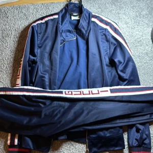Blå Gucci tracksuit - Gucci track jacket i marinblått med vita och röda ränder längs ärmarna och axlarna. Klassisk retrostil med dragkedja och ribbade muddar. Tillverkad i Italien och har en sportig vibe med snygga detaljer och logotypband. den va köpt för kanske 10 år sen i DK. Denna modellen är otroligt svår att hitta och det finns ändast i butikerna. Jag har tyvärr inga kvitton men du kan göra alla Authenitic checkar du vill. Den passar om du är 165-175. Köpt för 14999 danska.  