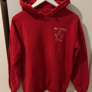 Röd hoodie från Gina Tricot med tryck - Röd hoodie från Gina Tricot med huva och snörning. På bröstet och ryggen finns tryck med texten 'MA CHÉRIE' och en stjärna. Mjuk insida och ribbade muddar vid ärmslut och nederkant. Som ny, tvättad en gång. 
