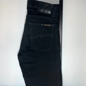 Nudie Jeans - Svarta jeans från Nudie Jeans med klassisk femficksdesign och diskret logga på bakfickan. Modellen är slim fit med smala ben och hög midja. Jeansen är tillverkade i stretchig bomullsdenim för en bekväm passform.