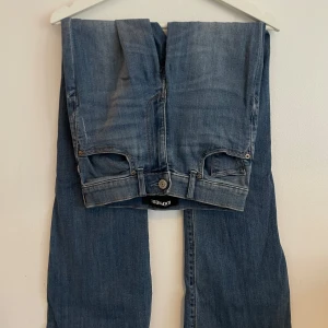 Express Bell Flare Medel Rise jeans - Snygga blå jeans från Express med bell flare-ben och medel hög midja. Jeansen har klassisk femficksdesign, stretchigt denimtyg och markerade sömmar. Perfekt för dig som gillar en retroinspirerad look med mycket vidd nertill.
