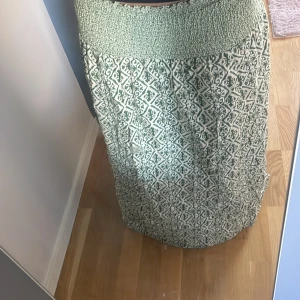 Grönvit långkjol med mönster - Säljer en långkjol i grönt och vitt med ett snyggt grafiskt mönster. Kjolen har bred smock i midjan för extra komfort och en luftig passform. Perfekt för dig som gillar bohemiska vibes och vill ha något bekvämt och stilrent.