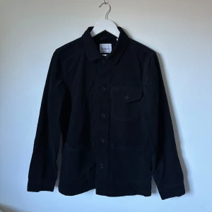 Svart overshirt från Lindbergh White - Svart overshirt från Lindbergh White i 100% bomull. Jackan har klassisk krage, knappstängning framtill, en bröstficka med knapp och två stora fickor nedtill. Perfekt för lager-på-lager och enkel att styla till jeans eller chinos. 3Y18