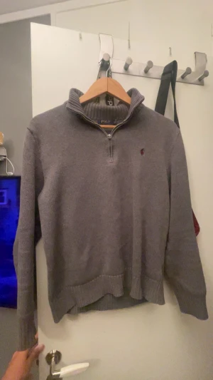 Grå stickad quarter zip tröja Polo Ralph lauren -  En stilren grå stickad tröja från Polo Ralph Lauren med halv dragkedja och hög krage. Klassisk broderad logga i vinrött på bröstet vilket jag tycker är väldigt snyggt. Tröjan har ribbade muddar och är långärmad, perfekt för kyligare dagar. Den hade passat perfekt från ca 160-166/7. Storlek s fast passar nog xs bättre.