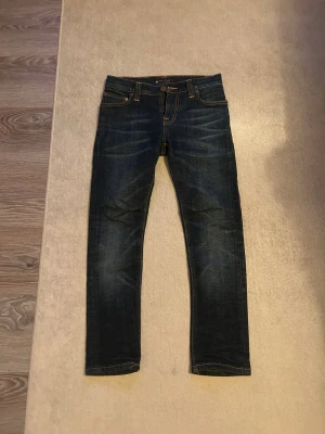 Mörkblå Nudie Jeans, slim fit - Snygga mörkblå jeans från Nudie Jeans med klassisk orange söm och broderade bakfickor. Modellen är slim fit med normal passform och raka ben. Tillverkade i ekologisk bomull för extra skön känsla och hållbarhet. Perfekt för dig som gillar stilrena jeans med coola detaljer.passar längd mellan 155-158