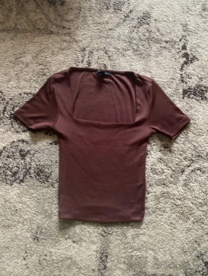 Brun topp med fyrkantig hals - Säljer en brun topp med korta ärmar och snygg fyrkantig halsringning. Toppens passform är tight och den är gjord i mjukt bomullsmaterial. Perfekt för dig som gillar minimalistisk stil och vill ha en enkel men trendig topp i garderoben.