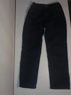 Svarta fina jeansbyxor - Säljer ett par svarta jeansbyxor med klassisk rak passform och normal midja. Byxorna har fem fickor och knappstängning framtill. Perfekta för dig som gillar enkel och stilren look.