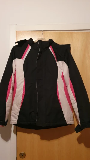 Vinterjacka - Cool vinterjacka från George i svart, rosa och vitt med snygga färgblock och huva med rosa fleecefoder. Jackan har dragkedja framtill, långärmade ärmar och justerbara muddar. Perfekt för kalla dagar när du vill ha både stil och värme. Det är i M i barn storlek. Har flera fläckar.