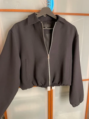 Svart bomberjacka från Zara - Svart bomberjacka från Zara med dragkedja framtill, klassisk krage och elastisk midja. Jackan har raka fickor och en stilren, minimalistisk look. Perfekt för dig som gillar en clean och modern stil.